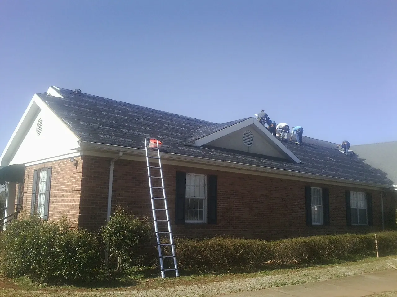 Crew tearing shingles off a brick ranch roof with a ladder set — Emergency Roof Repair work by our crew in Crooksville