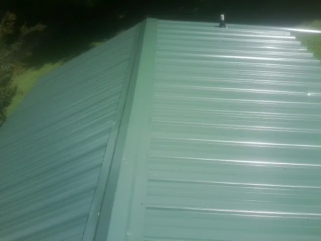 New green metal panels meeting at the ridge of a roof — Flat Roof Repair work by our crew in Crooksville