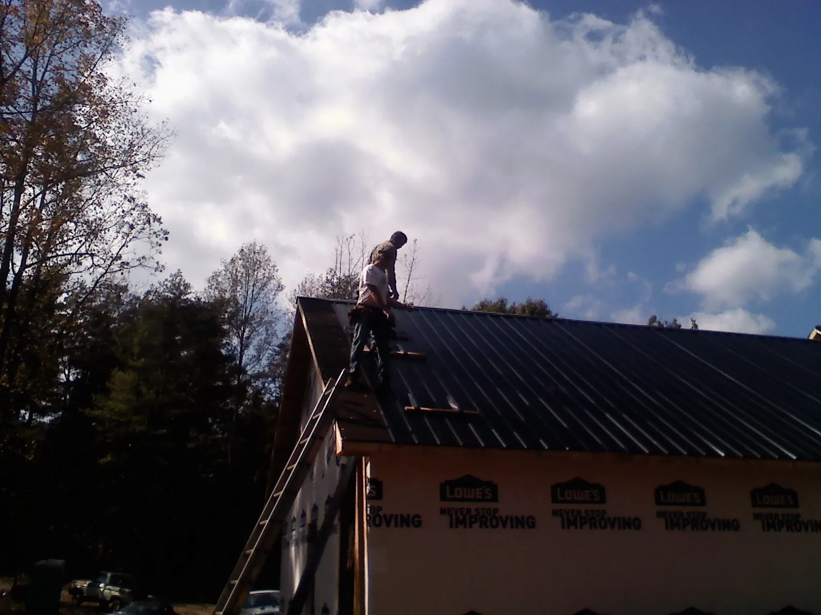 Roofer fastening dark metal panels high against a cloudy sky, from a Roof Inspection job in Crooksville