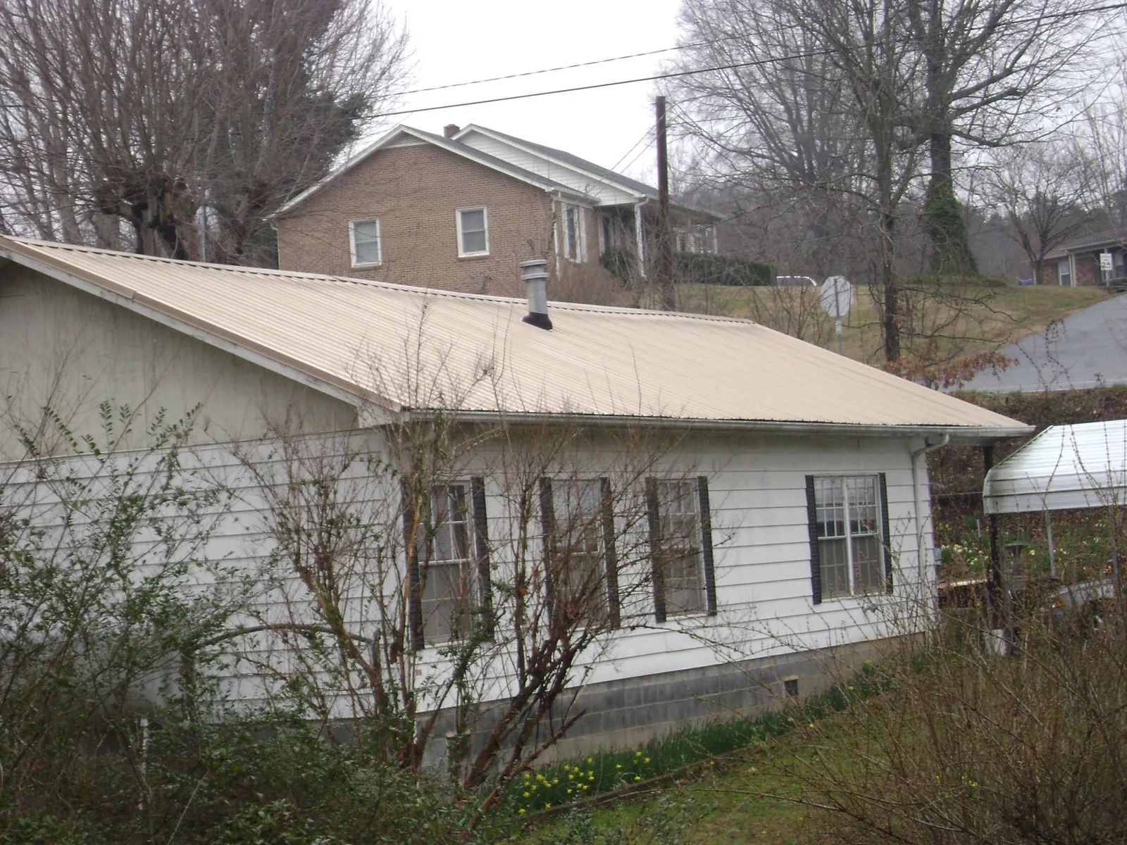 Tan metal roof on a white sided house set into a hillside — Commercial Roofing by Roofing Brothers in Crooksville